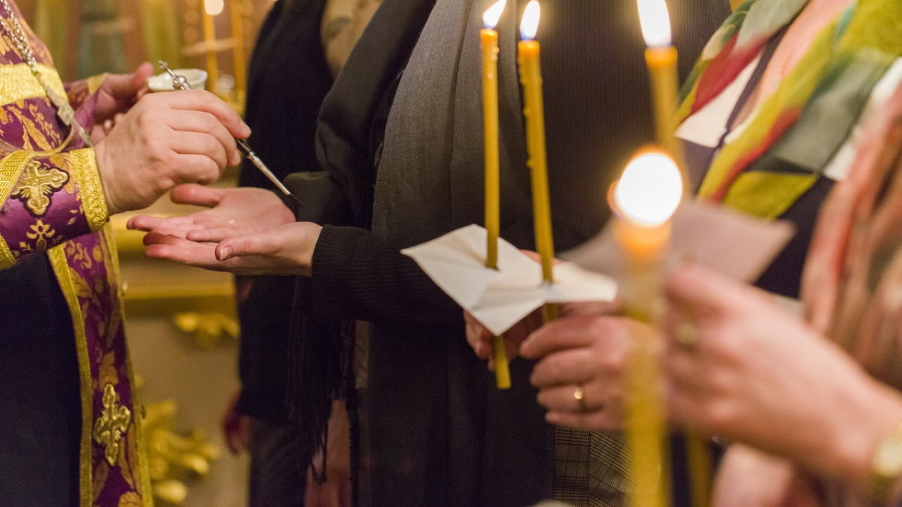Таинство соборования: руки со свечами, священник помазывает руки маслом