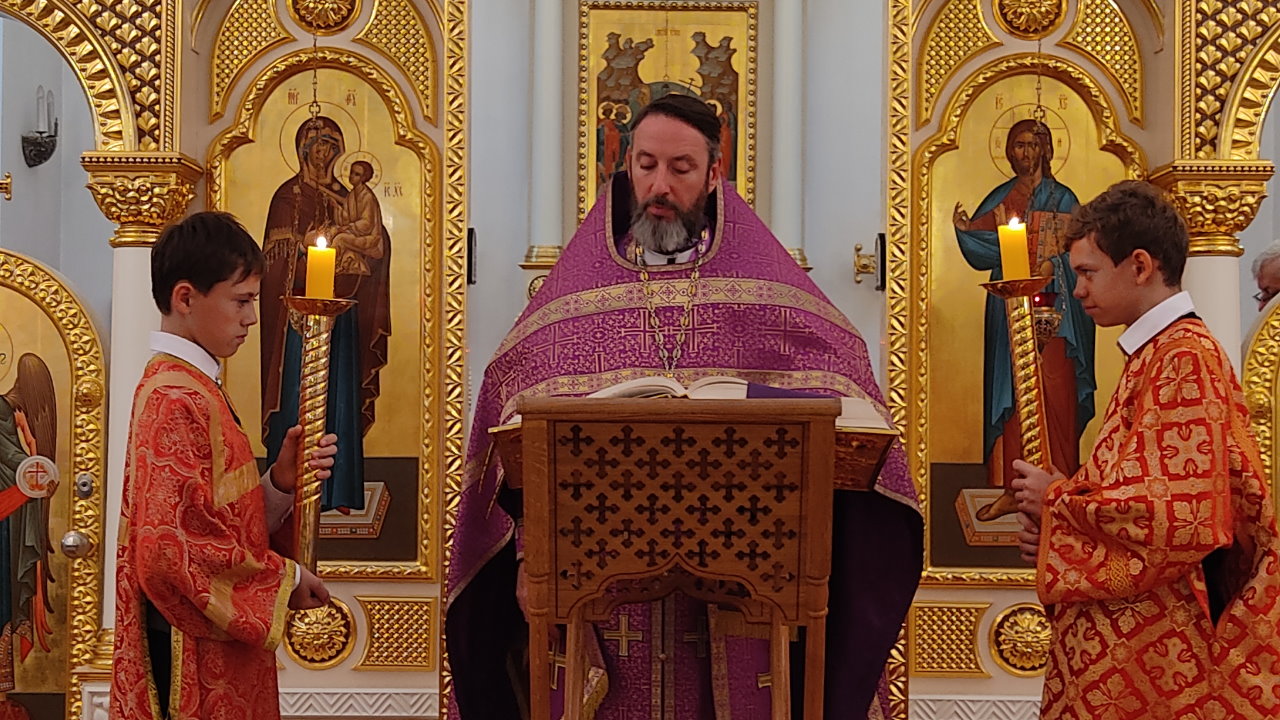 Священник Кирилл Краснощеков в фиолетовых одеяниях и 2 алтарника по бокам со свечами.