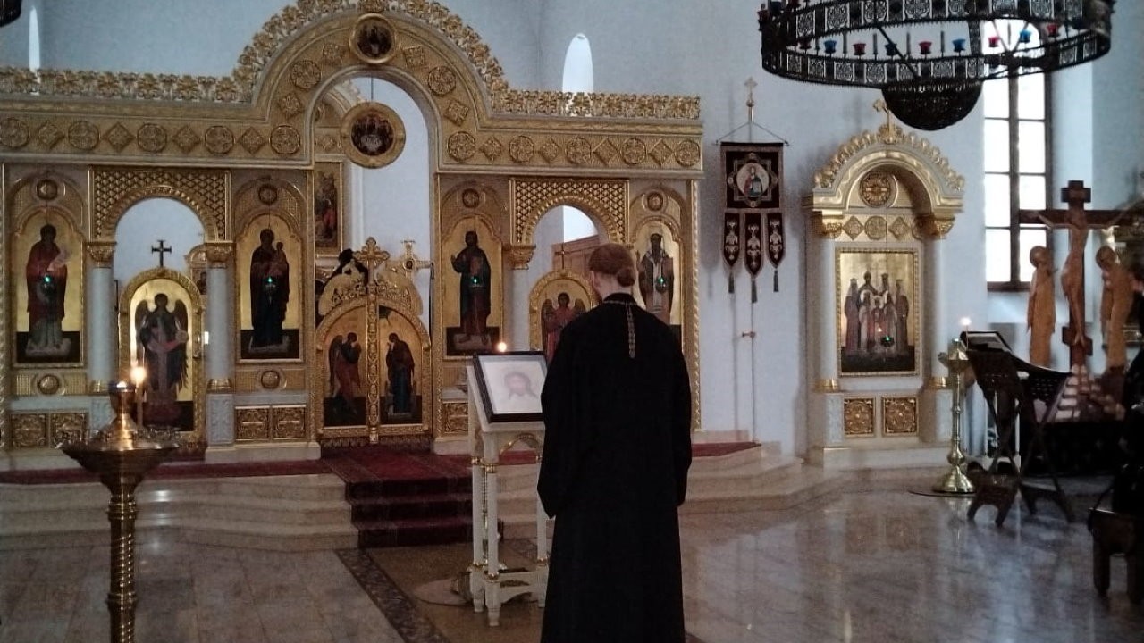 Священник в черном одеянии молится в храме