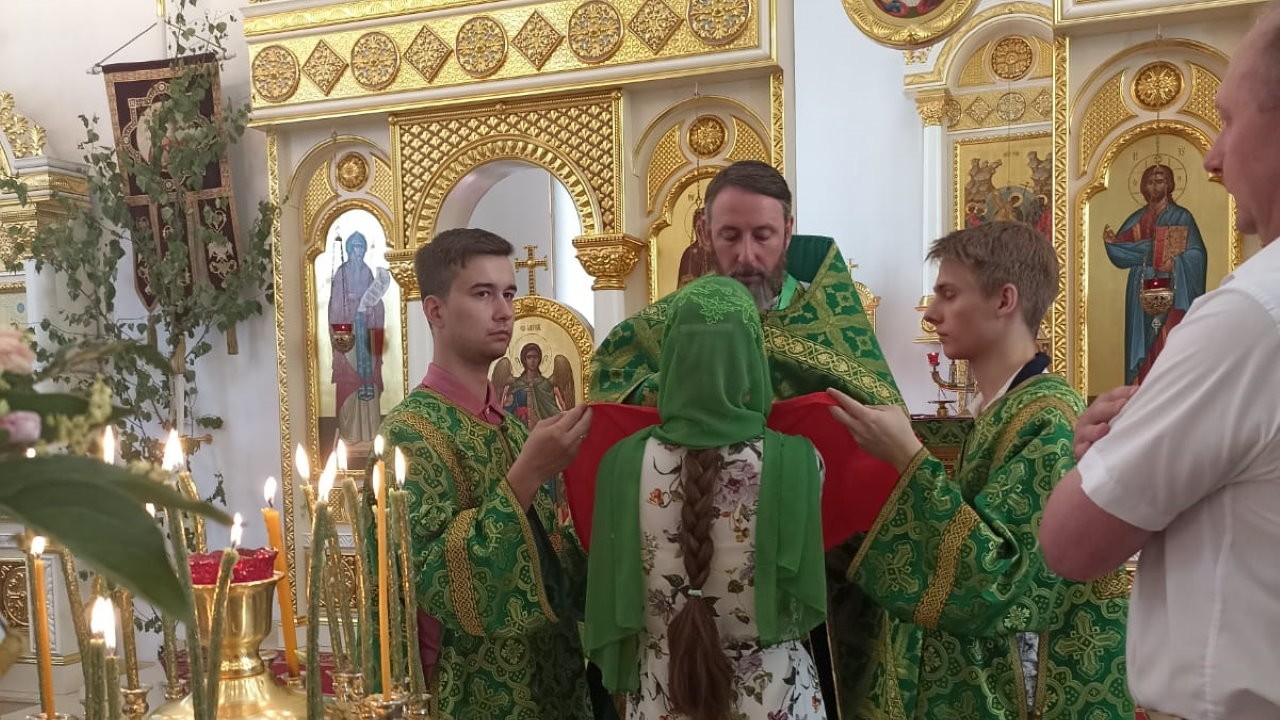 Протоиерей Кирилл Краснощеков в зеленых одеяниях причащает девушку в белом
