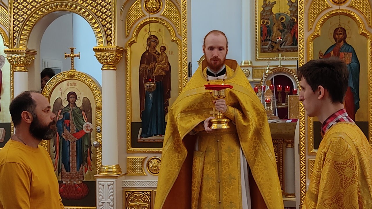 Священник Димитрий Попов в жёлтом облачении с Чашей в руках. По сторонам 2 алтарника.