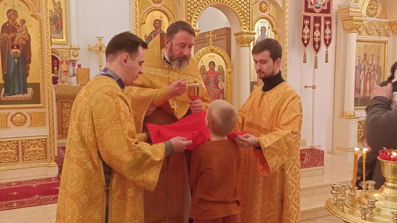Священник Кирилл Краснощёков причащает мальчика, 2 алтарника по сторонам 